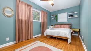 A bedroom with a bed, a ceiling fan, a window with curtains, and a wall-mounted shelf with decorative items. - Casa Cremosa (Hot Springs)