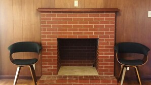 A room with a brick fireplace, two green chairs, and a wooden floor. - Casa Cremosa (Hot Springs)