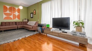A living room with a sectional sofa, a flat-screen TV, a wooden entertainment unit, and a patterned rug. - Casa Cremosa (Hot Springs)