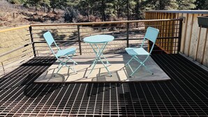 Een terras met metalen vloerplaten, een houten omheining en een tafel met vier blauwe stoelen.