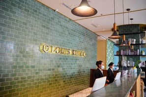 A reception area with a green tiled wall, a reception desk, and a shelf with various items. - Louis Kienne Hotel Pemuda (Semarang)