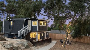 Une maison à deux étages, à l’extérieur sombre, dotée d’un patio couvert et d’une clôture en bois.