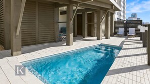 A swimming pool with a tiled deck, wooden pergola, and a view of a cityscape in the background. - Emerald Bluff, a premier Gulf Front home. Private Pool and Elevator by Kaiser Vacations. (Orange Beach)