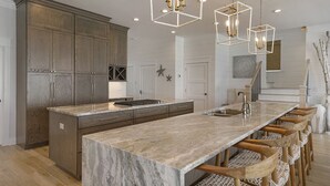 A modern kitchen with a large island, wooden cabinets, and pendant lighting. - A Gulf Dream - Gulf Front with Private Pool and Carriage House (Santa Rosa Beach)