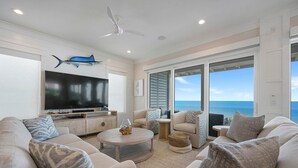 A spacious living room with a large flat-screen TV, comfortable seating, and a view of the ocean through large windows. - A Gulf Dream - Gulf Front with Private Pool and Carriage House (Santa Rosa Beach)