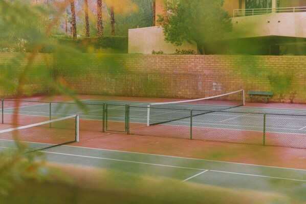 Ein Hallen-Tennisplatz mit Netz, Backsteinwand und einer Bank.