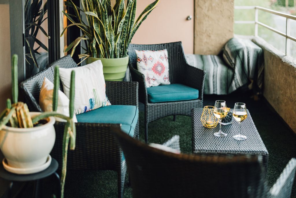 Un rincón al aire libre acogedor con mobiliario de mimbre, una silla verde acolchada y una mesa con copas de vino.