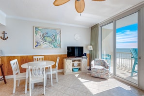Relax in this inviting living area with a view of the beach, featuring a dining table, TV, and comfortable armchair.