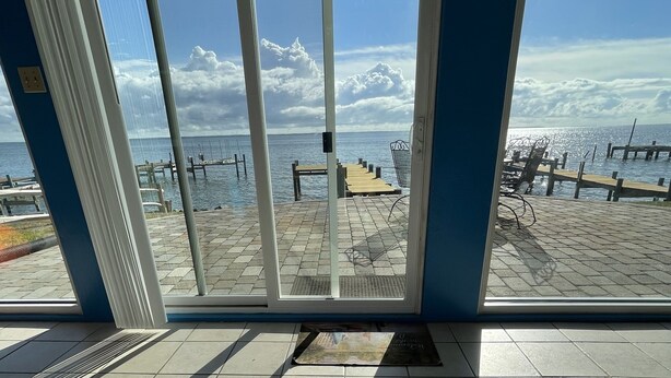 Une pièce dotée d’une grande fenêtre donnant sur une plage, avec une jetée en bois et des chaises longues.