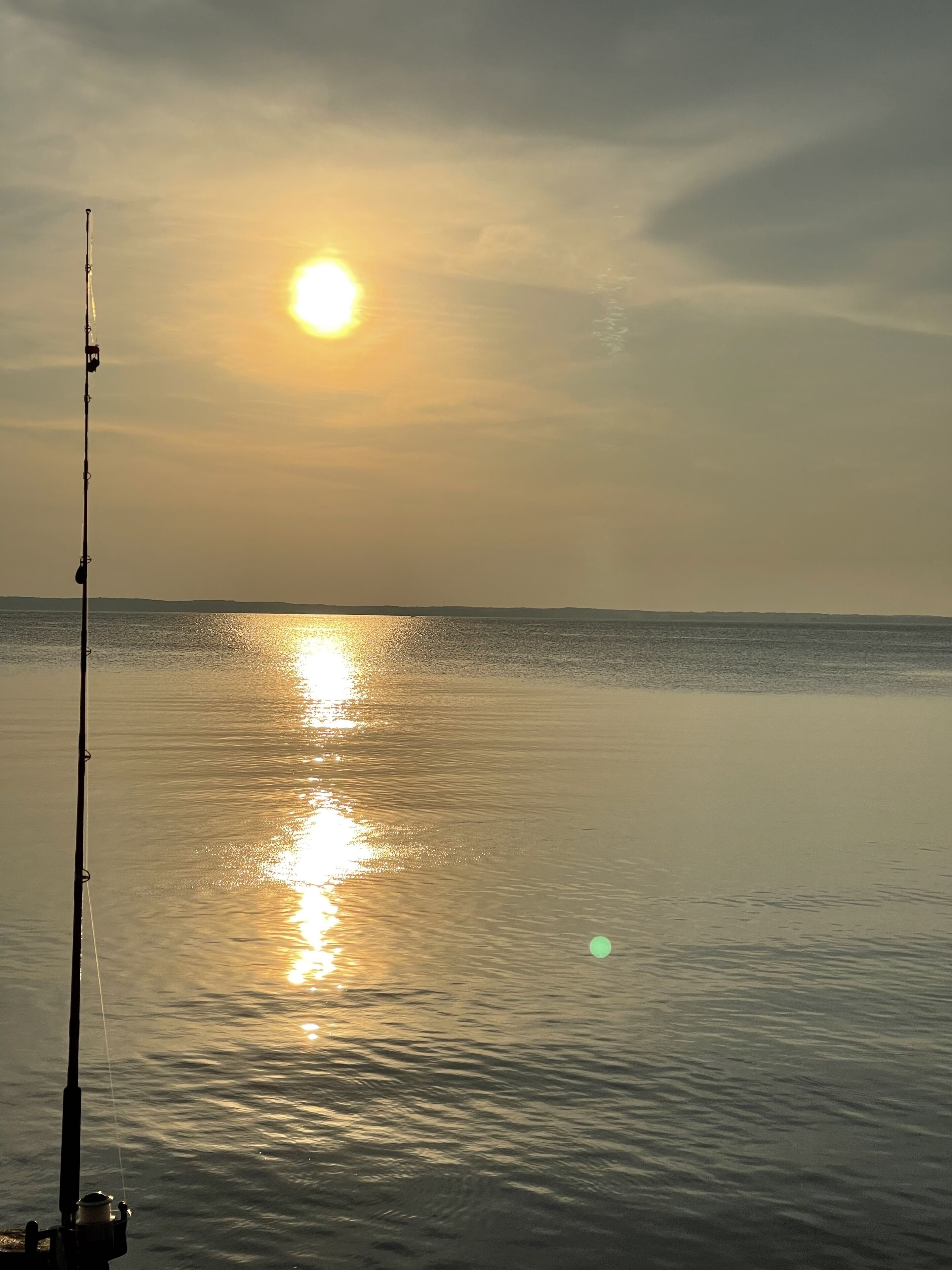 A fishing rod in calm water with a sunset in the background.