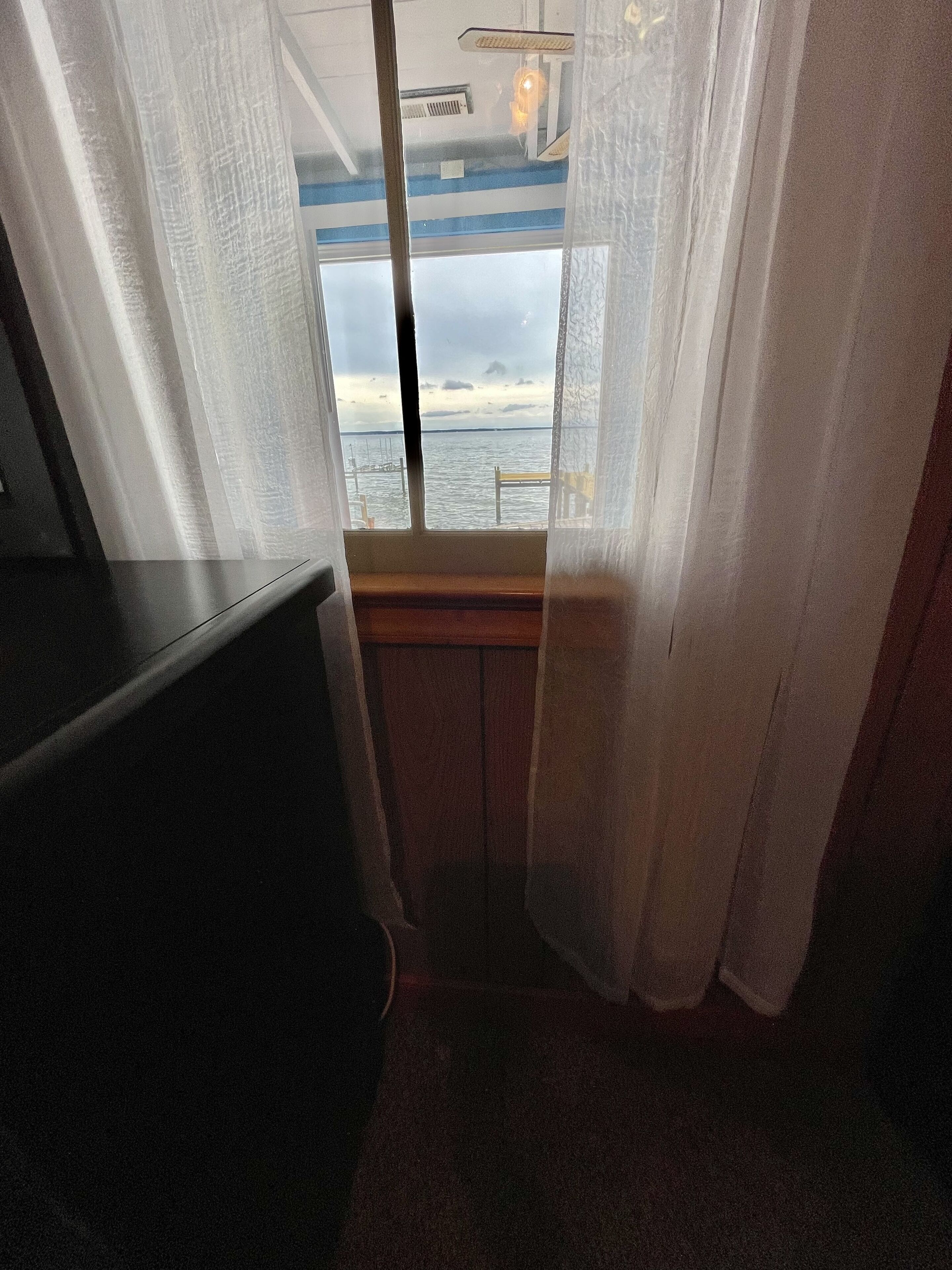 Una habitación con ventana que da a una masa de agua, un banco de madera y un ventilador de techo.