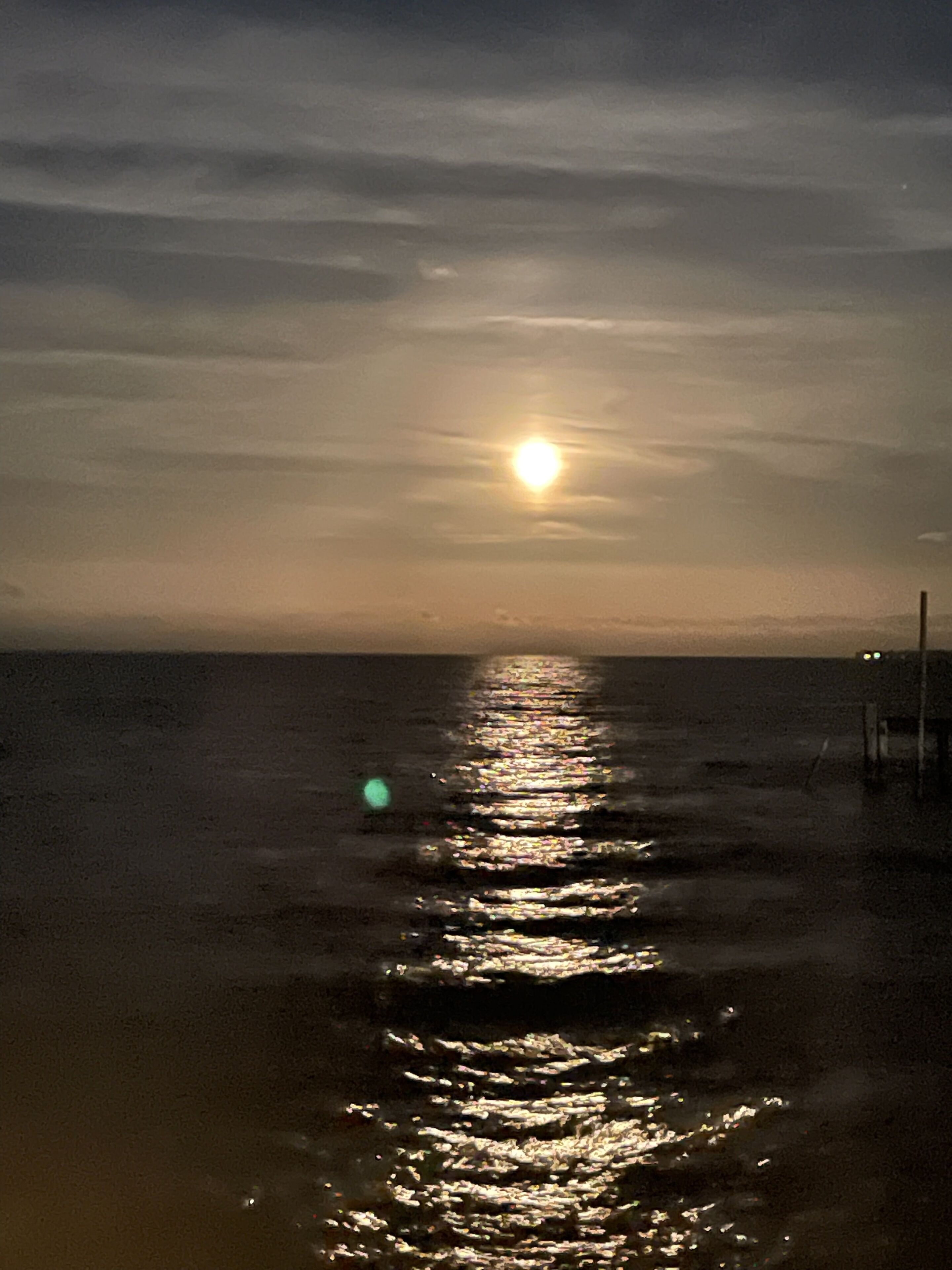 A beach scene with the sun reflecting on the water at sunset.