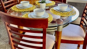 Une table ronde en verre, surmontée d’assiettes et de bols blancs, entourée de chaises en bois dotées d’assises rembourrées.