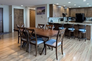 Cozinha moderna com armários de madeira, uma ilha central com banquetas e uma mesa de jantar com cadeiras.