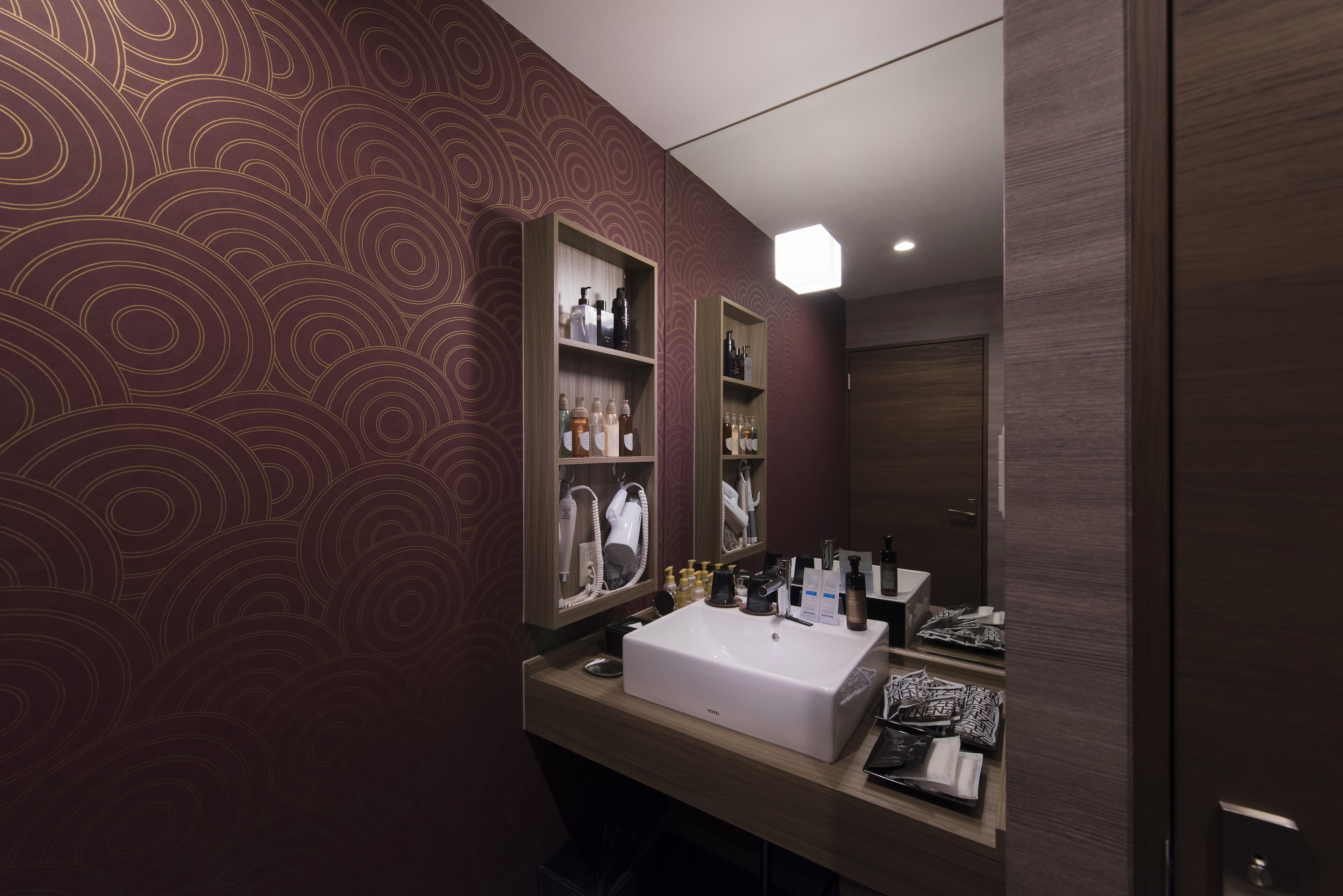 A modern bathroom with a large mirror, a white sink, and shelves with toiletries.