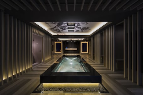 A modern, dimly lit hallway with a central pool, flanked by vertical paneling and recessed lighting.
