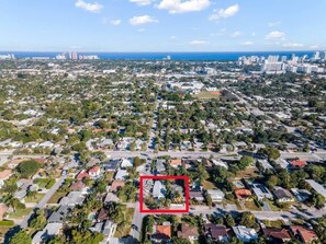 Residential neighborhood with single-family homes and apartment buildings, surrounded by trees and a coastline.