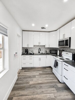 A modern kitchen with white cabinets, a microwave, a stove, and a tiled backsplash.