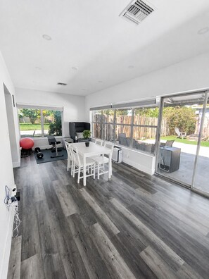 A spacious room with a large sliding glass door leading to an outdoor patio, a white dining table with chairs, and a red exercise ball. - Poinsettia Paradise  - 1 BDR Wing with Patio Near Beach (Fort Lauderdale)