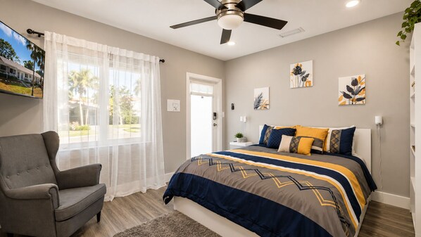 A bedroom with a bed, a chair, a ceiling fan, and artwork on the walls.