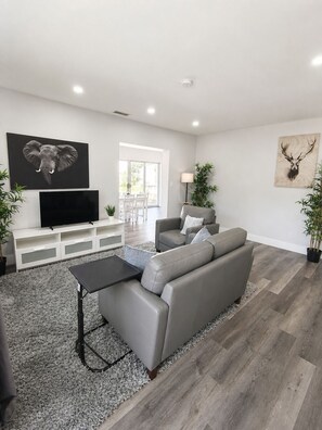 A modern living room with a grey sofa, a black coffee table, a flat-screen TV on a white entertainment unit, and artwork of an elephant and a deer head. - Poinsettia Paradise  - 1 BDR Wing with Patio Near Beach (Fort Lauderdale)
