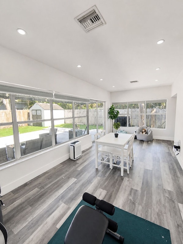 A spacious room with large windows, a dining table, a workout bench, and a grey bean bag.