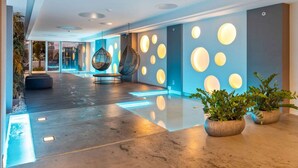 A modern lobby with a reflective floor, hanging chairs, and circular wall lights.