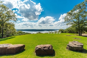 Ein grasbewachsenes Feld mit großen Steinen und Blick auf einen See sowie Berge in der Ferne.