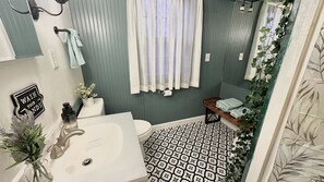 Ein Badezimmer mit einem weißen Waschbecken, einer Toilette, einer Badewanne, einem Duschvorhang und einer Sitzbank mit Handtüchern.