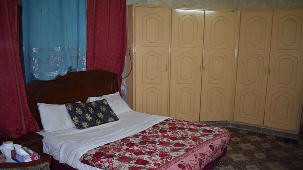 A bedroom with a bed, a wooden headboard, a floral bedspread, a wardrobe, and patterned carpet.