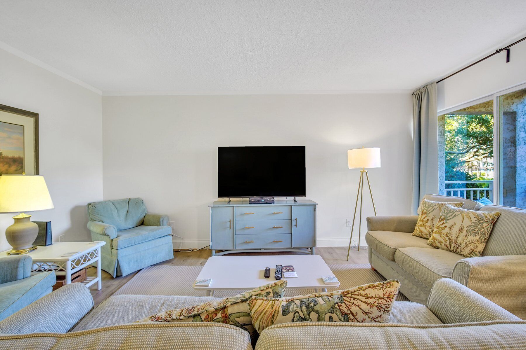 A living room with a flat-screen TV on a cabinet, a sofa, a coffee table, and a lamp.