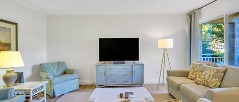 A living room with a flat-screen TV on a cabinet, a sofa, a coffee table, and a lamp.