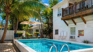 A swimming pool with a wooden deck, palm trees, and a white building with a balcony. - Old Town Key West Cottage (Naval Air Station Key West)