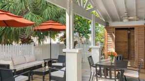 An outdoor patio with a white fence, wicker furniture, and wooden tables. - Old Town Key West Cottage (Naval Air Station Key West)