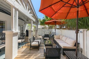 An outdoor patio with a white fence, wicker furniture, and orange umbrellas. - Old Town Key West Cottage (Naval Air Station Key West)