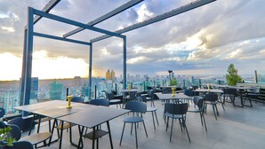 A rooftop dining area with tables and chairs, a metal framework, and a city view. - The Penthouse Residence (Phnom Penh)