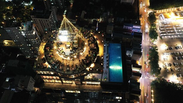 An aerial view of a cityscape at night with a prominent building featuring a circular plaza and a central structure with lights. - The Penthouse Residence (Phnom Penh)