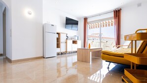 A modern hotel room with a kitchenette, a bed with a yellow headboard, a TV mounted on the wall, and a large window with curtains. - Las Floritas 23 Terrace and Swimming Pool (Playa de las Américas)