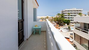 A balcony with a small table and a chair, overlooking a pool area with umbrellas and palm trees. - Las Floritas 23 Terrace and Swimming Pool (Playa de las Américas)