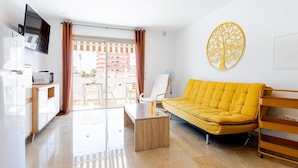 A modern living room with a yellow sofa, a flat-screen TV, a wooden coffee table, and a balcony with a view of buildings. - Las Floritas 23 Terrace and Swimming Pool (Playa de las Américas)