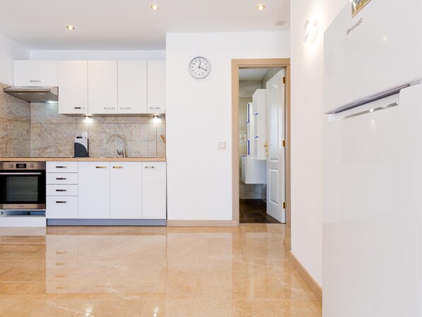 Una cocina moderna con armarios blancos, horno empotrado y campana extractora de acero inoxidable.
