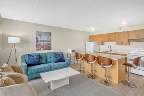 A modern kitchen with wooden cabinets, a white refrigerator, and a built-in island with bar stools. - Poolside Waikiki Banyan Condo with 2 Queen Beds and FREE Parking! (Honolulu)