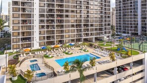 A multi-story hotel with a rooftop swimming pool, sun loungers, and a parking garage. - Poolside Waikiki Banyan Condo with 2 Queen Beds and FREE Parking! (Honolulu)
