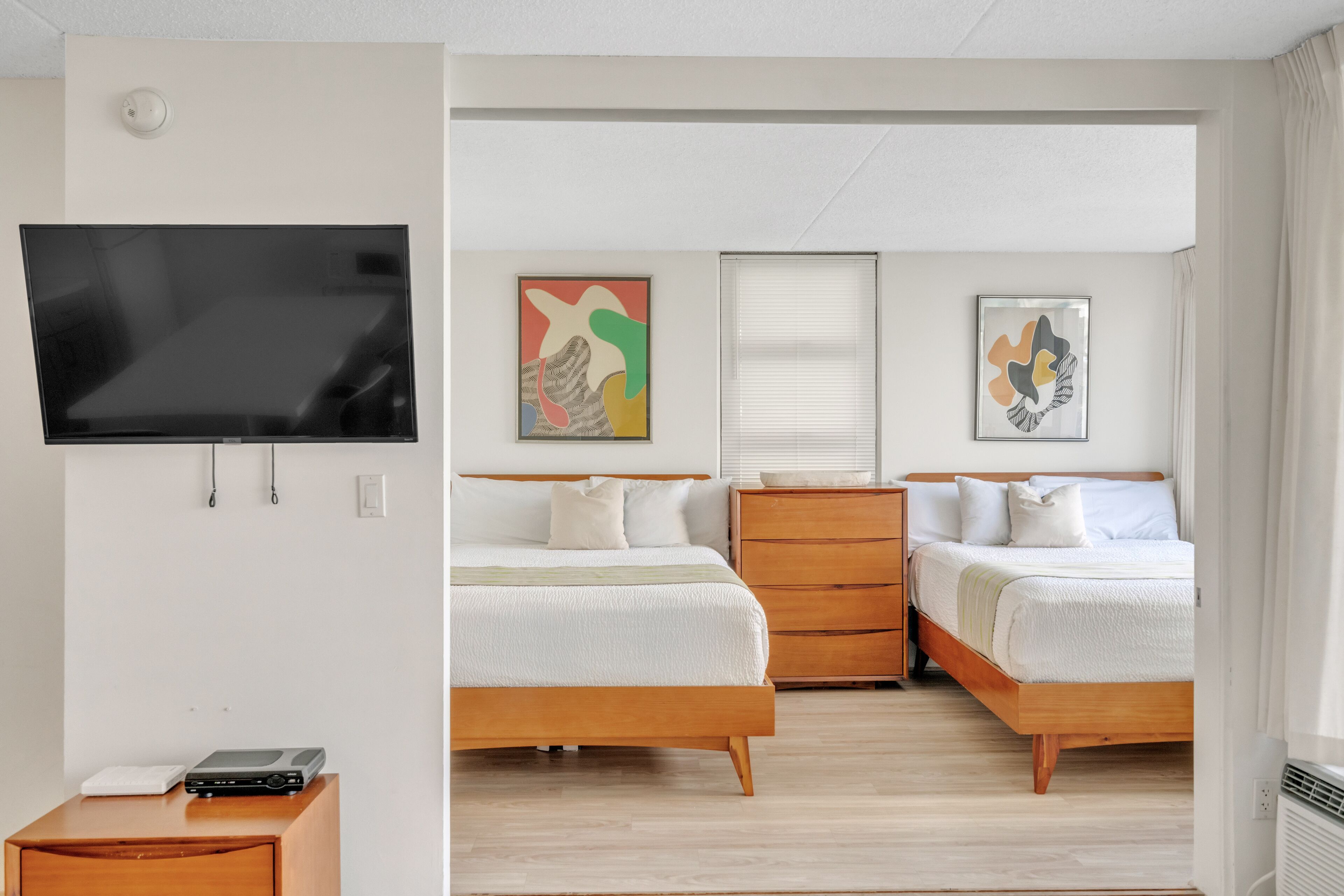 A hotel room with two beds, a TV, artwork on the walls, and a wooden dresser.
