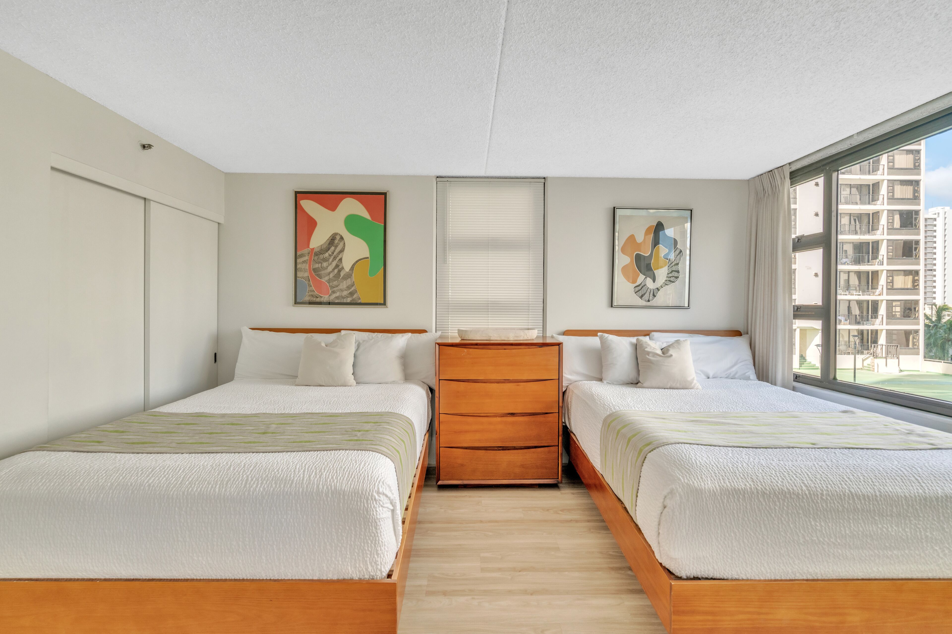 Una habitación de hotel con dos camas, un aparador de madera y obras de arte en las paredes.