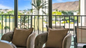 A balcony with two cushioned chairs and a table, overlooking a residential area with houses and a mountain in the distance. - Poolside Waikiki Banyan Condo with 2 Queen Beds and FREE Parking! (Honolulu)