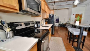 A modern kitchen with wooden cabinets, a stainless steel microwave, a black stove, and a refrigerator. - ★ THE PAD ★ KING BED ★ (Kansas City)