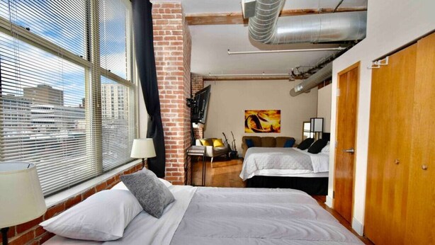 A hotel room with two beds, a brick wall, a window with blinds, and a city view. - ★ THE PAD ★ KING BED ★ (Kansas City)
