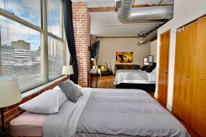 A hotel room with two beds, a brick wall, a window with blinds, and a city view. - ★ THE PAD ★ KING BED ★ (Kansas City)