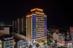 Un hotel de varios pisos con señalización iluminada, una entrada destacada y un entorno urbano circundante.